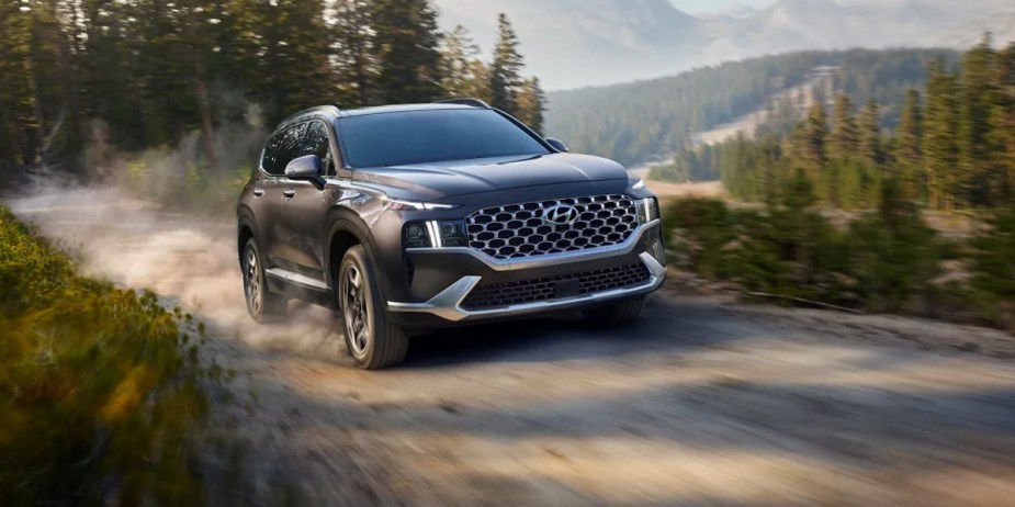 A gray 2023 Hyundai Santa Fe Hybrid midsize hybrid SUV is driving on the road. 