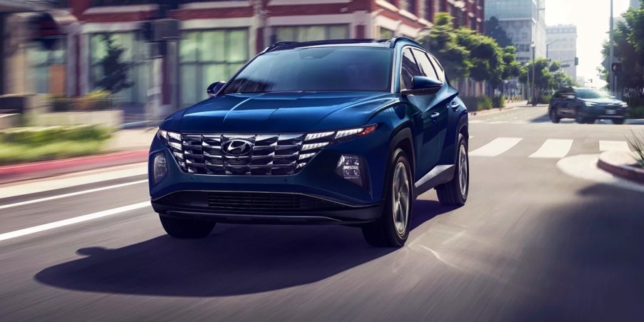 A blue 2023 Hyundai Tucson Hybrid small hybrid SUV is driving on the road.