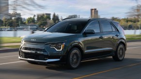 A green 2023 Kia Niro subcompact hybrid SUV is driving on the road.