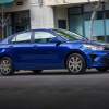 A blue 2023 Kia Rio subcompact car travels on a city street