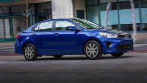 A blue 2023 Kia Rio subcompact car travels on a city street