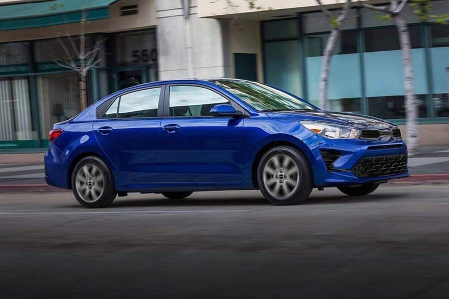 A blue 2023 Kia Rio subcompact car travels on a city street