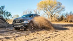 Silver Ram 1500 rebel speeding along a sandy off-road trail, trees visible in the background.