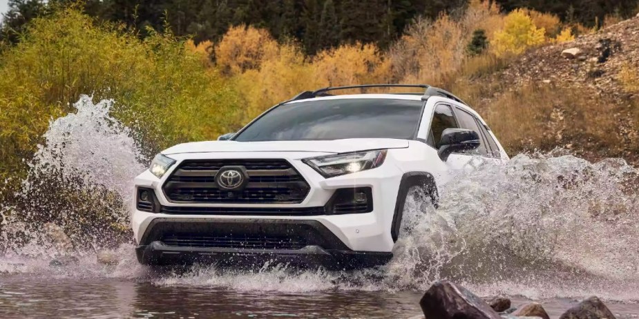 A white 2023 Toyota RAV4 small SUV is driving through the water. 