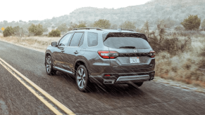 A rear shot of a 2024 Honda Pilot Elite midsize SUV in Modern Gray Metallic driving through desert rain