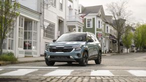 A 2024 Kia Seltos subcompact SUV model in Pluton Blue stopped at a cobblestone crosswalk