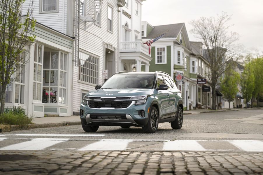 A 2024 Kia Seltos subcompact SUV model in Pluton Blue stopped at a cobblestone crosswalk