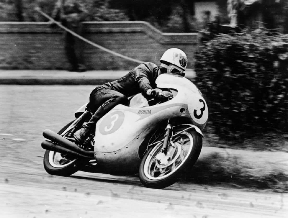 A black and white motorsport photo shows Bob McIntyre leaning a Honda at the Isle of Man TT. 