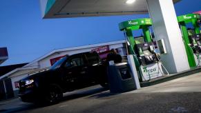 Man gases up his black Silverado pickup truck at a station that sells diesel, the sunset visible in the background.