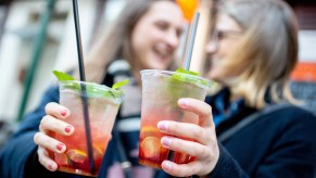 Two women toast with alcoholic cocktails to go.