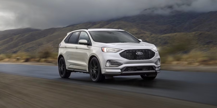 A white Ford Edge midsize SUV is driving on the road.