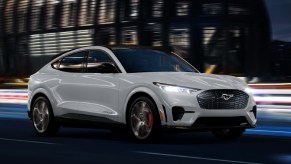 A white 2023 Ford Mustang Mach-E small electric SUV is driving on the road.