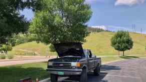 This is Henry Cesari's black 1988 Ford F-150 in a parking lot with its hood up for repairs it's an example of an 80s and 90s truck.