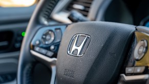 Close-up of Honda logo on steering wheel of a vehicle, with vehicle interior visible. Honda sales have made these models more popular