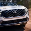 A white 2023 Hyundai Santa Fe midsize SUV is driving on the road.