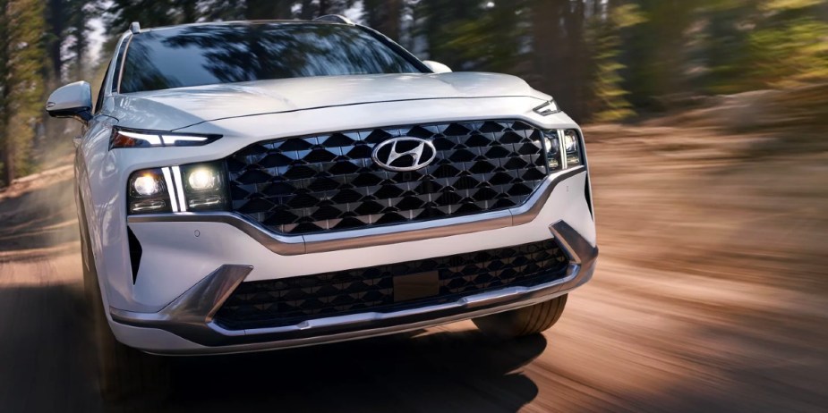 A white 2023 Hyundai Santa Fe midsize SUV is driving on the road. 