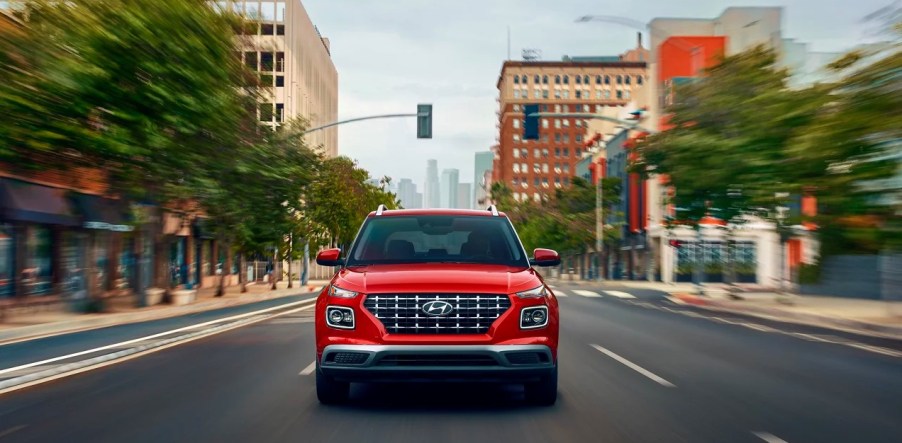 A red 2023 Hyundai Venue subcompact SUV is driving on the road.