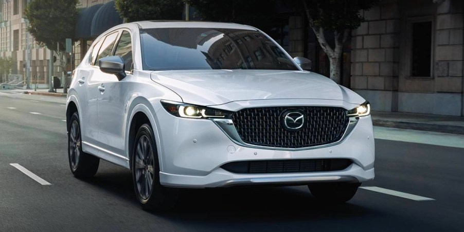 A white 2024 Mazda CX-5 small SUV is driving on the road.