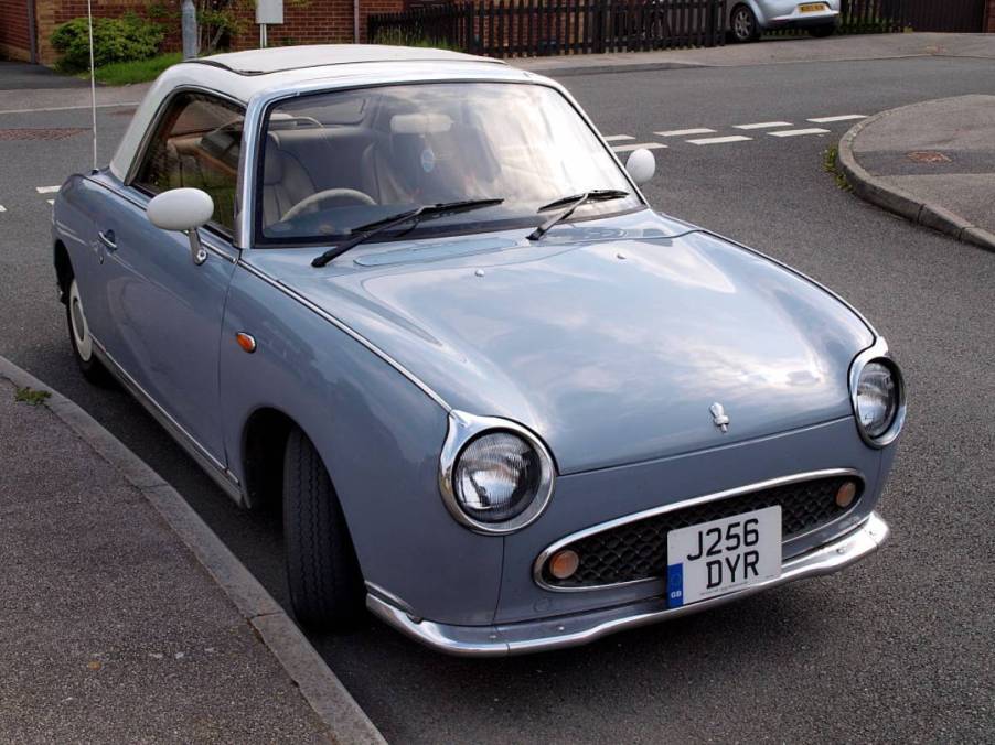 A Nissan Figaro parked on the side of the street.