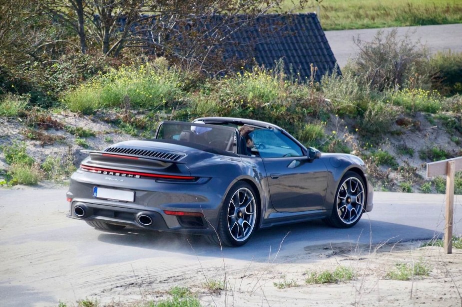 Black Porsche convertible driving along a dirt road.