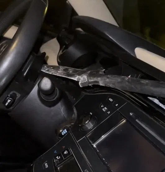 the tip of a spear through through a woman's windshield is stuck in the back of her steering wheel.