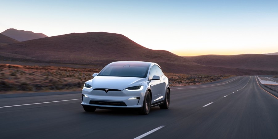 A white Tesla Model X midsize electric SUV is driving on the road.