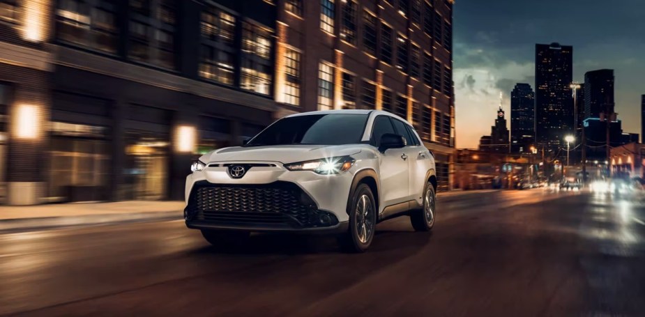 A white 2023 Toyota Corolla Cross subcompact SUV is driving down the road at night. 