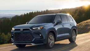 A blue 2024 Toyota Grand Highlander three-row midsize SUV is driving on the row.