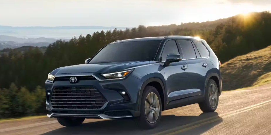 A blue 2024 Toyota Grand Highlander three-row midsize SUV is driving on the row. 