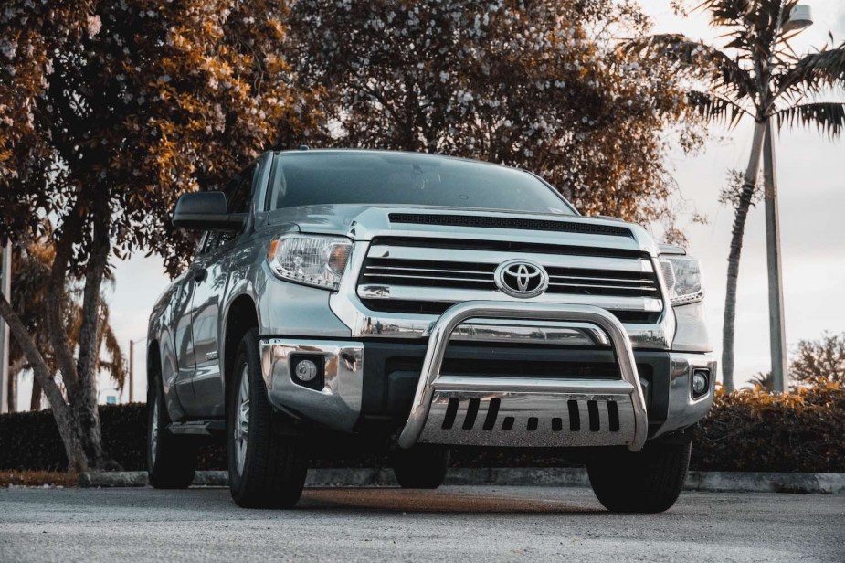 The chrome grille of a 2nd-generation used Toyota Tundra pickup truck, worth $25k, parked in front of palm trees.