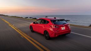 A rear side shot of a 2024 Subaru Impreza RS hatchback model driving on a highway past the sea