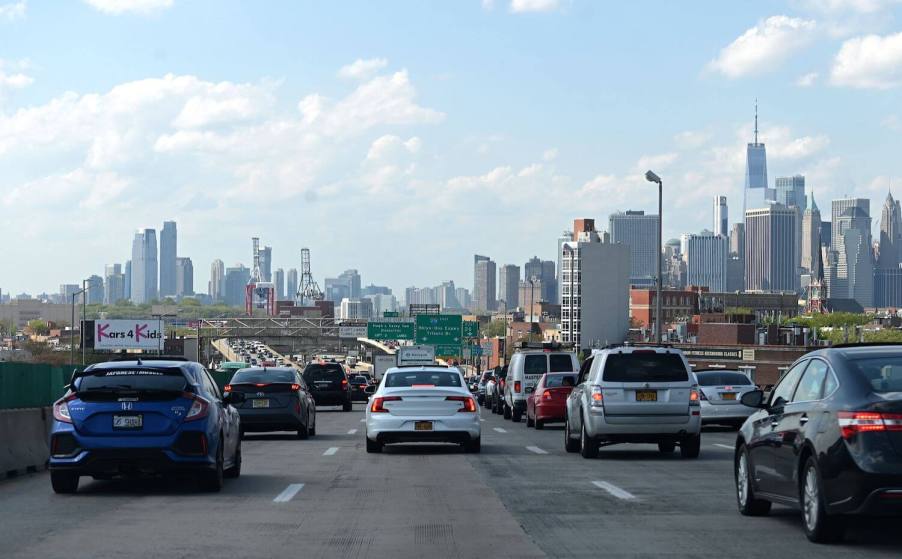 A row of cars waiting in stop-and-go traffic, the Manhattan skyline visible behind.