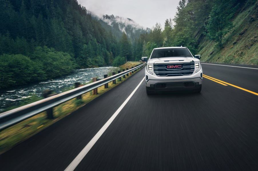 A 2024 GMC Sierra 1500 SLT Crew Cab Short Box 4WD full-size pickup truck model driving past a forest river