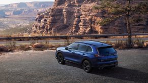 A blue Honda CR-V Sport Touring parked in front of a cliff. Many are choosing to buy a Honda CR-V now.