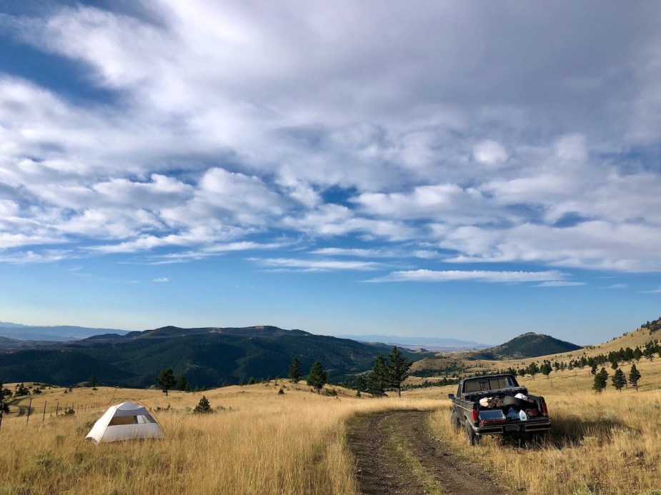 Black Ford pickup truck parked by a National Park trail with a tent set up nearby for overlanding camping.