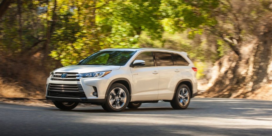 A white 2018 Toyota Highlander Hybrid midsize hybrid SUV in motion. 