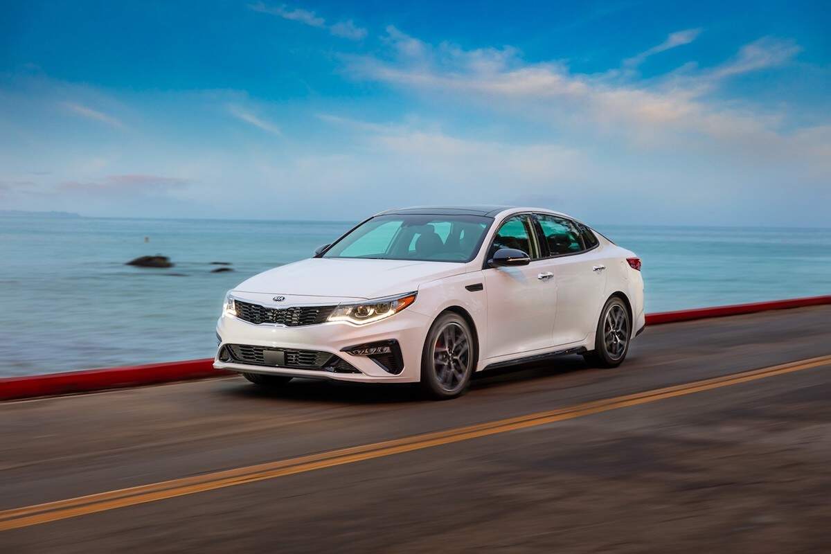 A white 2020 Kia Optima driving on a road along a beach