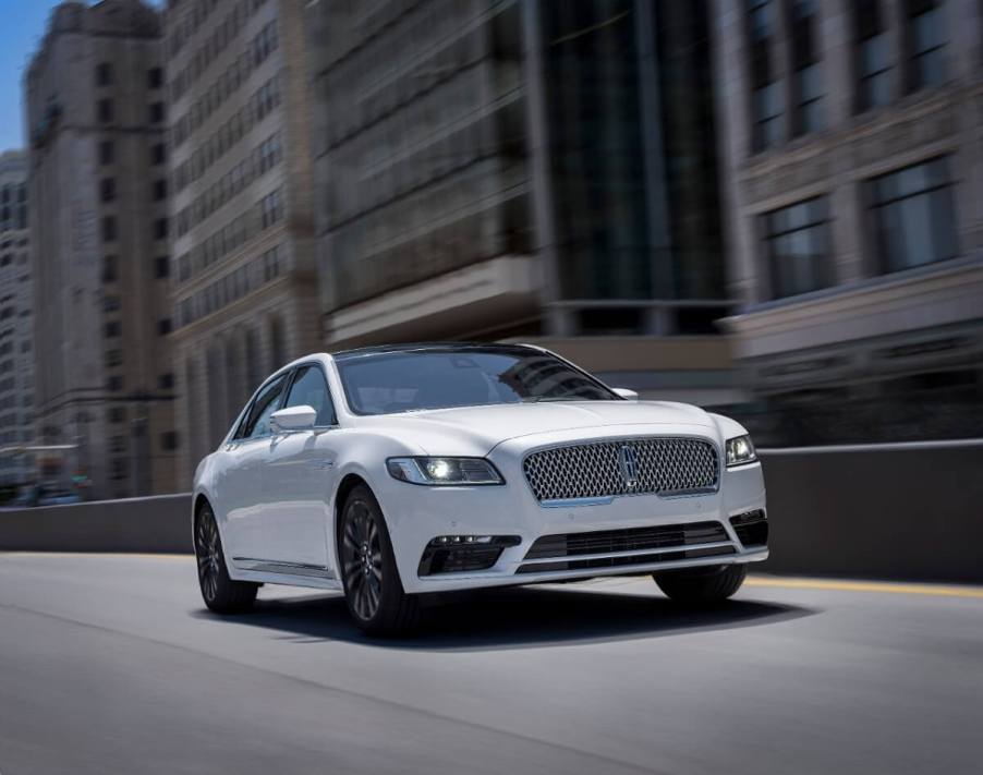 A used white Lincoln Continental luxury car cruises down city streets.