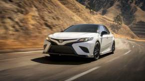 A white 2020 Toyota Camry travels on a mountain highway