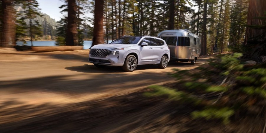 A white 2023 Hyundai Santa Fe midsize SUV is driving off-road.