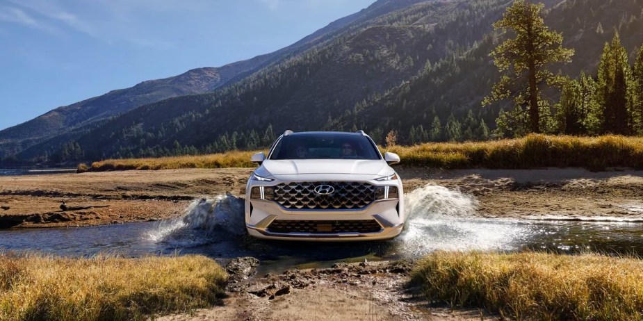 A white 2023 Hyundai Santa Fe midsize SUV is driving through water. 