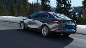 A 2023 Mazda3 sedan drives down a snowy road