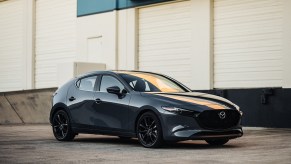 A black 2023 Mazda MAzda3 Hatchback front 3/4 shot at sunset in an industrial complex