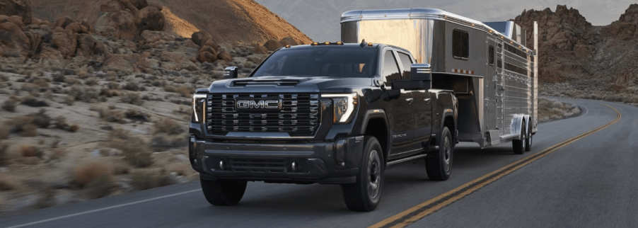 A 2024 GMC Sierra 3500 HD Denali Ultimate model towing a shiny camper trailer on a desert highway