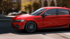 A side profile shot of a 2024 Honda Civic Hatchback model in Rallye Red driving through a city