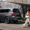 A side profile shot of a parked 2024 Infiniti QX80 full-size luxury SUV model as people walk toward it