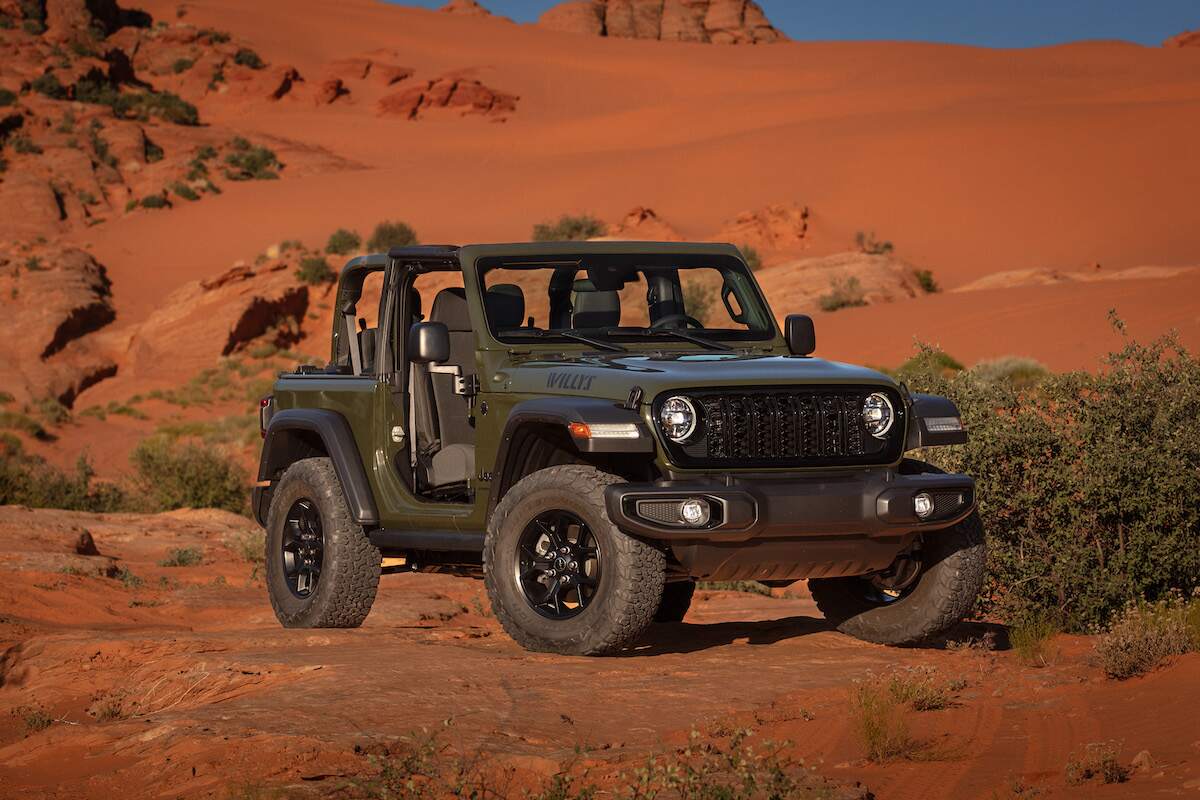 A dark-gray 2024 Jeep Wrangler Willys 2-door parked in front of a dusty red hill