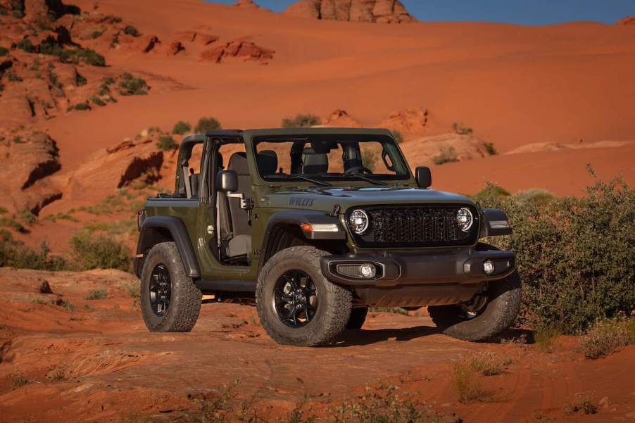 A dark-gray 2024 Jeep Wrangler Willys 2-door parked in front of a dusty red hill