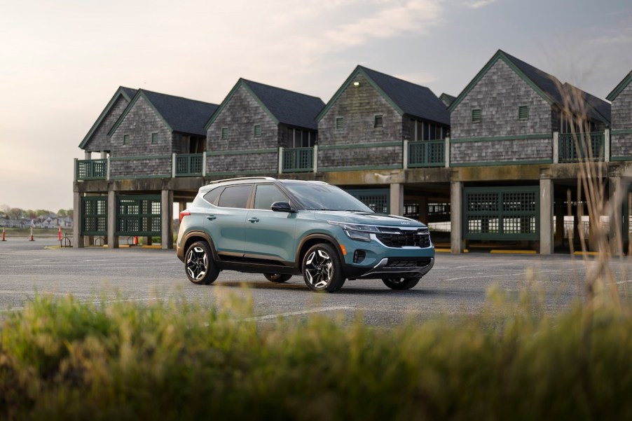 A 2024 Kia Seltos in Photon Blue near the beach and some elevated buildings. The 2024 Kia Seltos' price is an attractive point.