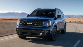 A blue 2024 Kia Telluride driving on an open road.